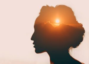 A composite silhouette of a woman with the sun rising above the clouds in her head.