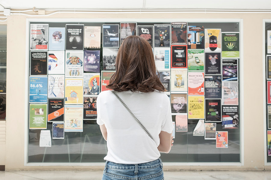 A young woman checking an announcement board filled with flyers.