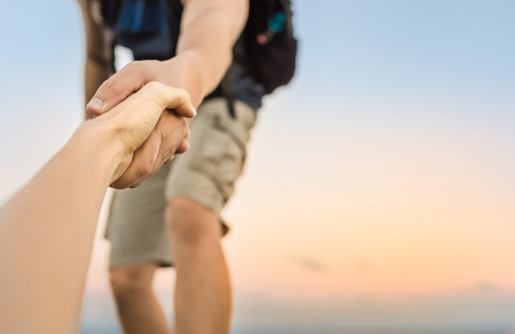 A hiker firmly grasping the hand of their companion and helping them.